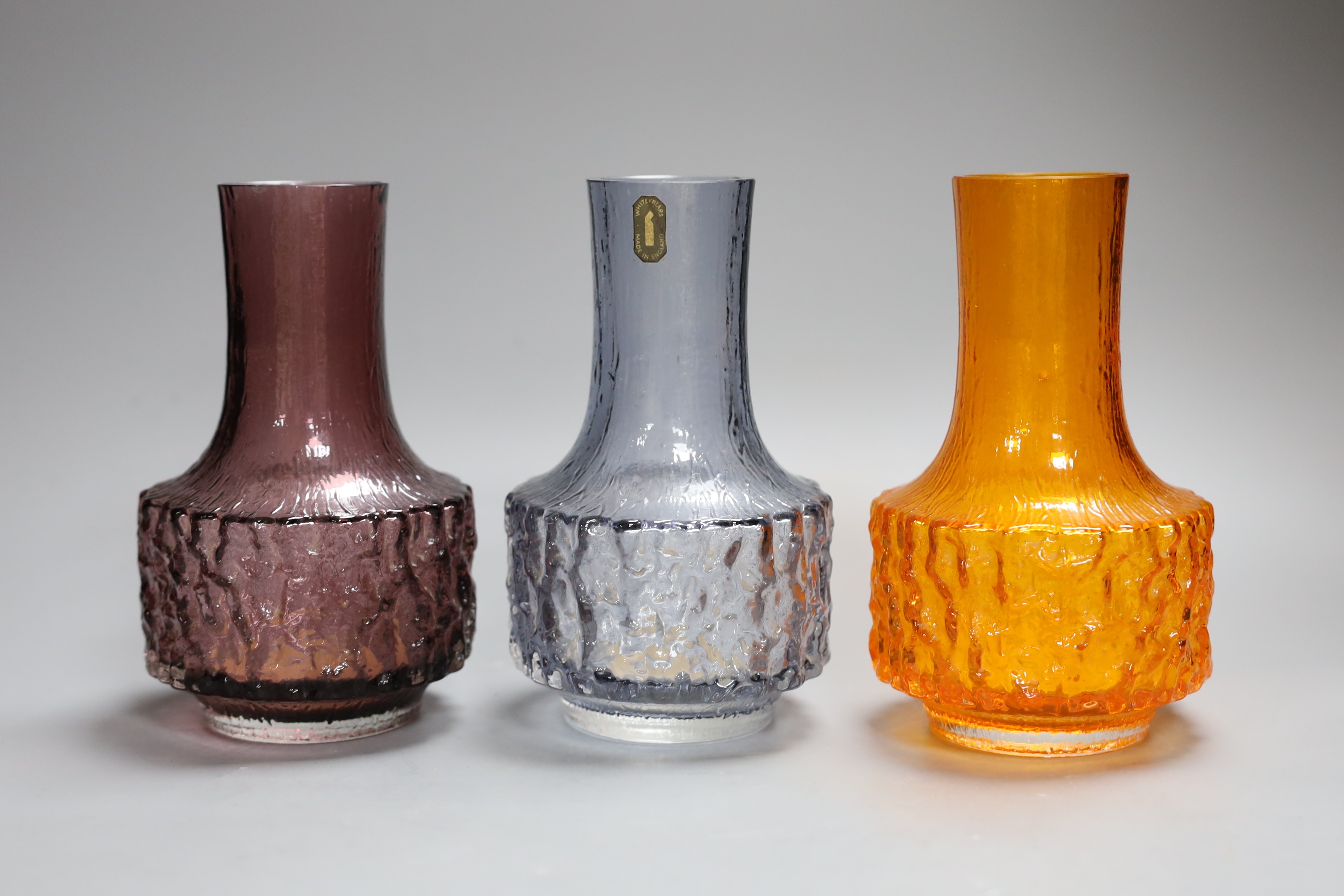 Three Whitefriars cylindrical bottle vases, in amethyst, tangerine and smoked glass, each 18cm high.